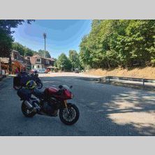 Czerwony motocykl zaparkowany na postoju w Serbii, w otoczeniu lasu i budynków z wieżą — miejsce odpoczynku uczestników wyprawy Caravana wyjazdy motocyklowe.