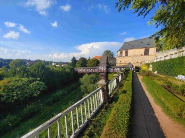 Historyczny kompleks budynków z drewnianym mostkiem i ogrodami, położony nad zieloną doliną w Czechach