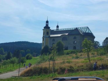 Kościół na wzgórzu z dwiema wieżami i przeszklonym dachem, otoczony zielenią w Czechach