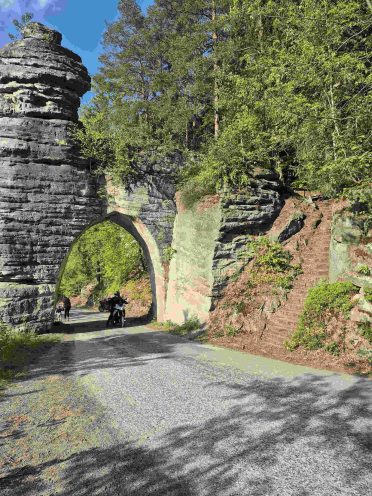 Motocykle przejeżdżające pod naturalną skalną bramą na leśnej trasie w Czechach – wyprawa motocyklowa