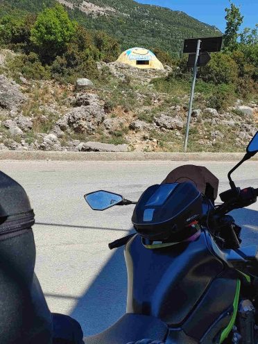 Motocykl przy głazie z napisem Amfilochia podczas wyprawy motocyklowej po Bałkanach, malownicza trasa w Grecji.